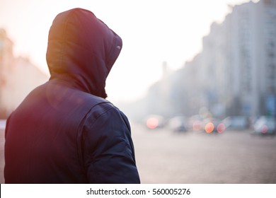 Hipster man in hood walking on city street in the evening