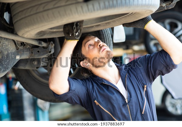 Hipster man mechanic working Under a Vehicle in a\
Car Service station. Expertise mechanic working in automobile\
repair garage.