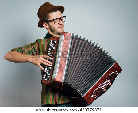hipster man plays on the bayan, wearing a hat and glasses, isolated on a gray background
