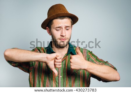 hipster man showing good or bad, wears glasses and hat, isolated on gray background