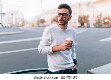 Hipster Man Standing With Takeaway Coffee, Smiling Plesantly, Walking On Th City Street. Happy Carefree Handsome Guy In Eyewear. Millennial Generation