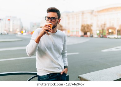 Hipster Man Standing With Takeaway Coffee, Smiling Plesantly, Walking On Th City Street. Happy Carefree Handsome Guy In Eyewear. Millennial Generation