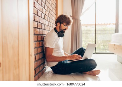 Hipster man using laptop and sitting on floor at home. Online shopping, home work, freelance, online learning, studying concept. Distance education.