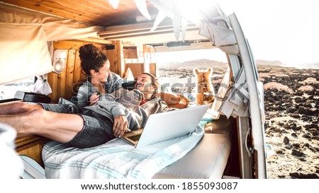 Hipster man and woman with dog traveling together on mini van transport - Freelance nomad concept with hippie people on minivan romantic trip working at laptop pc in relax moment - Warm retro filter