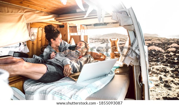 Hipster man and woman with dog traveling together\
on mini van transport - Freelance nomad concept with hippie people\
on minivan romantic trip working at laptop pc in relax moment -\
Warm retro filter