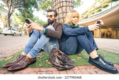 Hipster millennial couple in disinterest moment with smartphone - Apathy concept about sadness and isolation using mobile smart phone - Millenial boyfriend and girlfriend with cellphone addiction