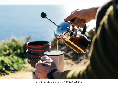 Hipster millennial man with hand tattoos prepare specialty coffee in french press, use camping stove and enamel cup. Good filter coffee during camping trip - Powered by Shutterstock