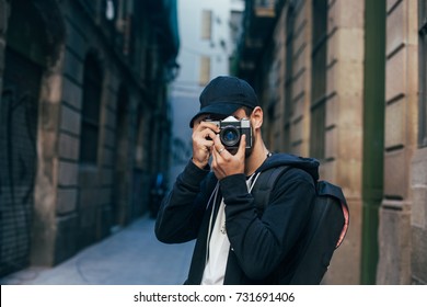 Hipster millennial young man or teenager with analog vintage photo camera makes photograph into lens in middle of old town or city with sunset light, explores tourism - Powered by Shutterstock