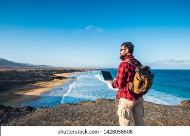 Hipster people using outdoor cimputer laptop with internet connection for work or to communicate at home - traveler with backpack and alternative travel vacation - beach and sea in background