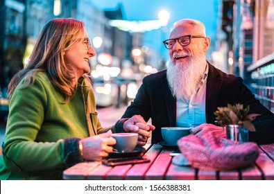 Hipster retired senior couple in love enjoying cappuccino at outdoor cafeteria - Joyful elderly lifestyle concept with wife and husband having fun at bar cafe restaurant - Vivid neon lights filter