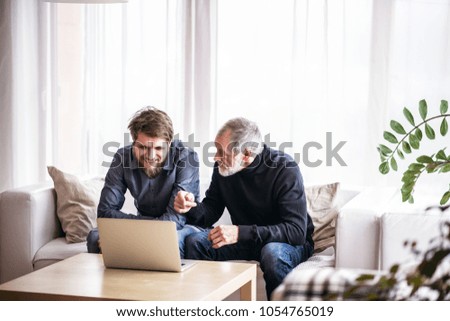 Hipster son and his senior father with laptop at home.