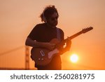 Hipster street musician in black playing electric guitar in street outdoors on sunset