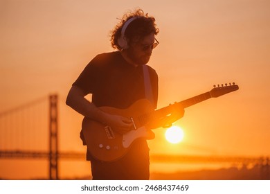 Hipster street rock musician in black playing electric guitar in street outdoors on sunset - Powered by Shutterstock