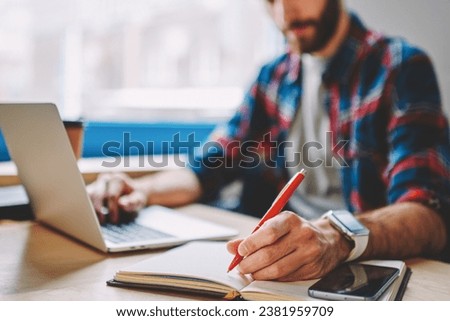 Hipster student making notes in notepad while working at netbook