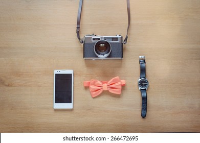 Hipster style. Overhead of Different photography objects on wooden background. Items include retro camera, smart phone, bowtie, watch.
