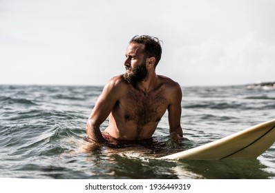 Hipster surfer sitting on his surfboard into the ocean water and waiting for a big wave - Fit bearded man training with surfboard to sea - Adventure and freedom concept doing water extreme sports - Powered by Shutterstock