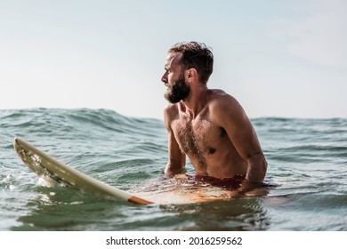 Hipster surfer sitting on his surfboard into the ocean water and waiting for a big wave - Fit bearded man training with surfboard to sea - Adventure and freedom concept doing water extreme sports - Powered by Shutterstock