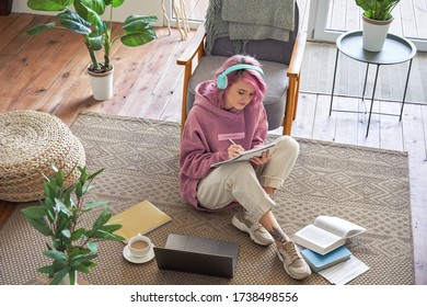 Hipster Teen Girl School College Student Pink Hair Wear Headphones Writing Notes Video Conferencing On Laptop Sit In Cozy Room On Floor Working Learning Online In Internet Watching Webinar. Top View.