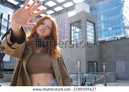 Hipster teen stylish redhead fashion girl model posing in big city urban location. Beautiful teenage generation z girl with red hair wearing trench coat looking at camera. Portrait
