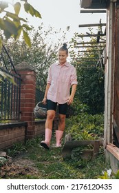 Hipster Trendy Millennial Woman In Pink Rubber Boots Holding Basket Of Red Ripe Tomato At Vegetable Garden Greenhouse. Fall Summer Harvest Season. Agriculture Eco Friendly Natural Organic Food Produce