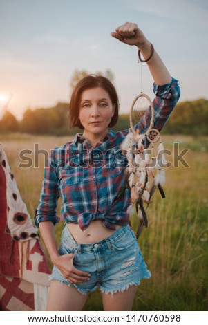 hipster woman in the form of a Shaman is looking for inspiration from the dream catcher in a wigwam in nature. Prayer, fantasy, sunset