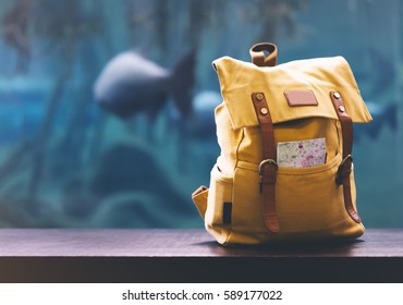 Hipster yellow backpack and map closeup. View from front tourist traveler bag on background blue sea aquarium. Person hiker visiting ocean museum in Barcelona on backdrop, blank blurred mock up