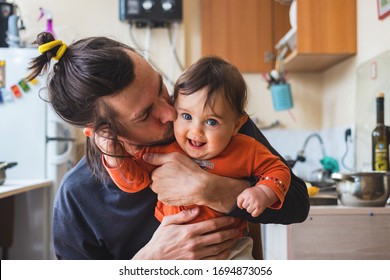 Hipster young father hug and kiss his baby infant boy holding on hands. At home on kitchen background. Lifestyle photo of family care and happiness concept. Middle class.  - Powered by Shutterstock