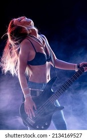 Hipster young female rock star guitarist performing on stage with head thrown back and long hair flying back against the light in a smokey atmosphere