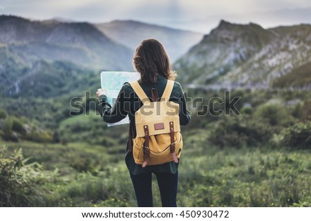 Hipster young girl with  backpack enjoying sunset on peak of mountain, looking map. Tourist traveler on background valley landscape  view mockup, sunlight in trip in  basque country, mock up for text.