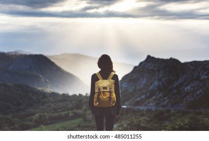 Hipster young girl with bright backpack enjoying sunset on peak of foggy mountain. Tourist traveler on background valley landscape view mockup. Hiker looking sunlight flare in trip Picos de Europa