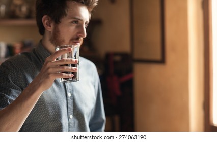 Hipster Young Man Drinking A Glass Of Coke And Looking Away Next To A Window