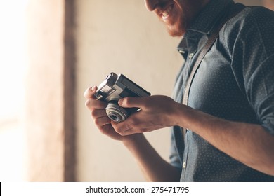 Hipster Young Man Holding A Vintage Camera And Checking Settings