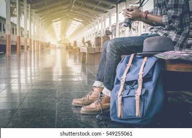 Hipster young man sitting hand holding camera and travel bag at the train station.