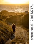 Hirtshals, Denmark A woman walks in silhouette towards a North Sea beach at sunset through a dune landscpe.