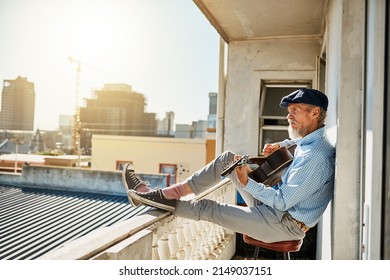 His daily ritual of playing guitar. Shot of a peaceful senior man sitting on his balcony while playing acoustic guitar with the city in the background. - Powered by Shutterstock