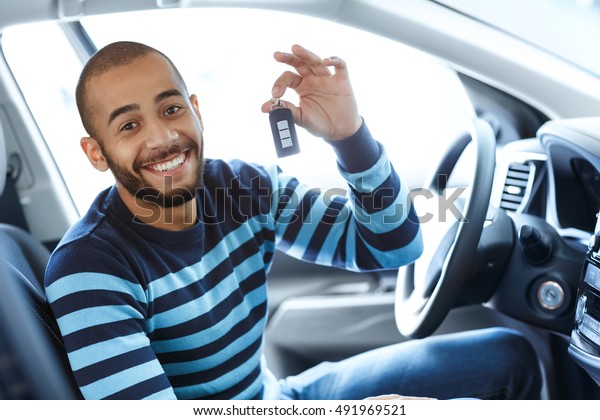 His dream day. Portrait of a handsome African man\
smiling excitedly while sitting in his newly bought car showing car\
keys to the viewer 