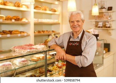 His hobby became his career. Happy senior man smiling leaning on the showcase while working at his own bakery running his small business copyspace - Powered by Shutterstock