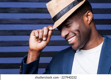 In his own unique style. Handsome young African man adjusting his hat and smiling while standing against striped background