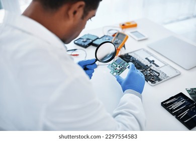 His problem solving skills and precision make him the pro. a young man using a magnifying glass while repairing computer hardware in a laboratory.