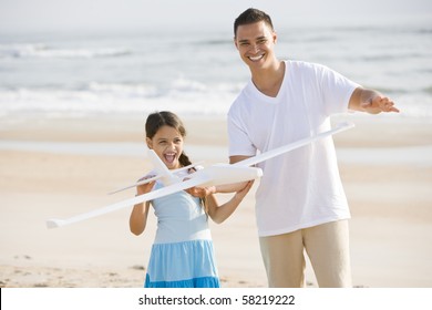 Hispanic 9 Year Old Girl And Father Playing With Toy Airplane On Beach