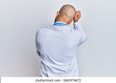 Hispanic adult man wearing doctor uniform and stethoscope backwards thinking about doubt with hand on head 
