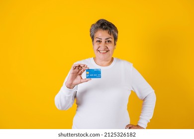 Hispanic Adult Middle Age Woman Holding Blue Credit Card Isolated Over Yellow Background In Latin America