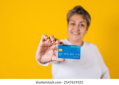 Hispanic Adult Middle Age Woman Holding Blue Credit Card Isolated Over Yellow Background In Latin America