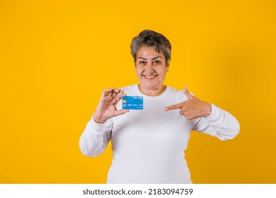 Hispanic Adult Middle Age Woman Holding Blue Credit Card Isolated Over Yellow Background In Latin America