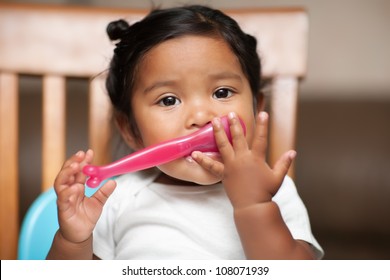 Hispanic Baby Girl Learning To Hold A Spoon By Herself