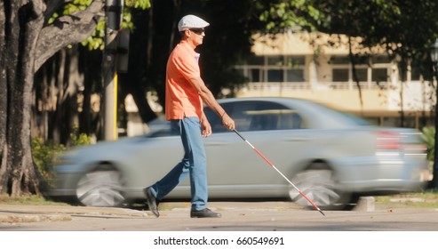 Hispanic blind man, latino people with disability, handicapped person and everyday life. Visually impaired man with walking stick, crossing the street with cars and city traffic