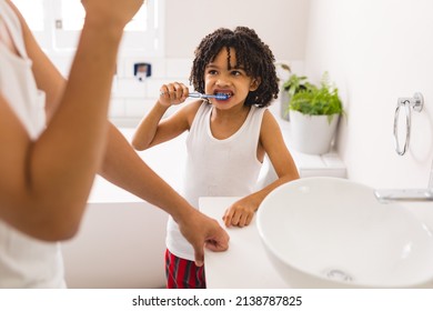 Hispanic Boy Brushing Teeth While Looking At Father Standing By Sink In Bathroom. Unaltered, Family, Togetherness, Hygiene And Routine Concept.