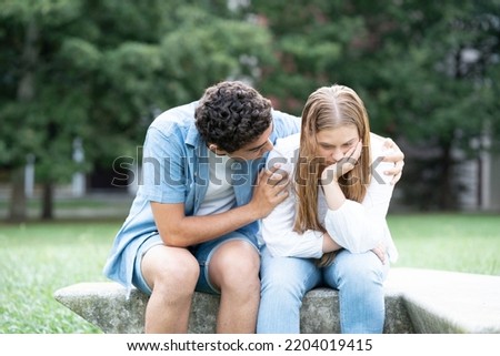 Hispanic boy comforting and hugging sad girfriend outdoors in a park.