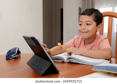 Hispanic boy with distance education - happy child doing his homework - Latin boy learning with books and his digital tablet at home - Powered by Shutterstock