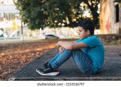 Hispanic Boy Sitting On Some Ruins Looking At The Horizon, With A Sad Expression.